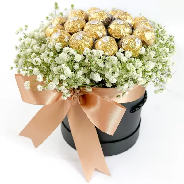 Round black box with white flowers and gold-wrapped Ferrero Rocher chocolates, tied with a rose gold bow.