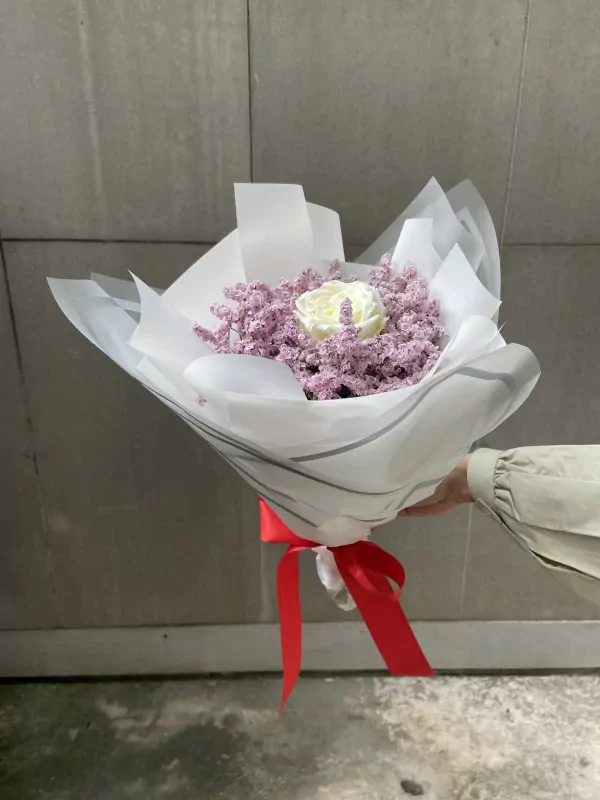 Bouquet of pink limonium with a single white rose, wrapped in white paper and tied with a red ribbon.