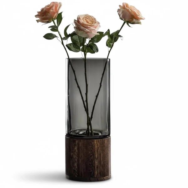 Three light pink roses in a grey glass vase with a dark wood base.