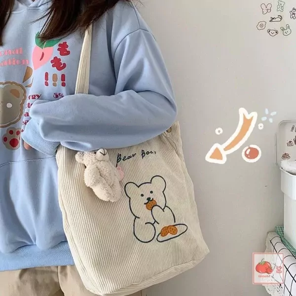 Cream corduroy tote bag with a drawn teddy bear and "Bear Boo" text. A small plush bear charm hangs from the strap.