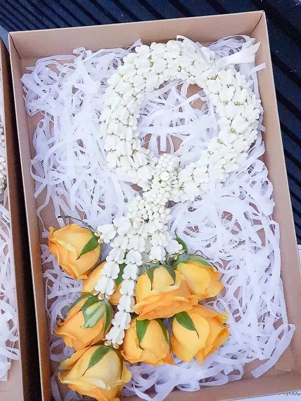 Yellow roses and white jasmine malai in a gift box with white shredded paper.