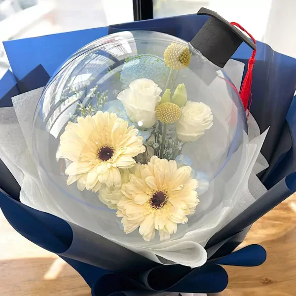 Graduation bouquet with flowers in a clear balloon, topped with a black graduation cap and red tassel.