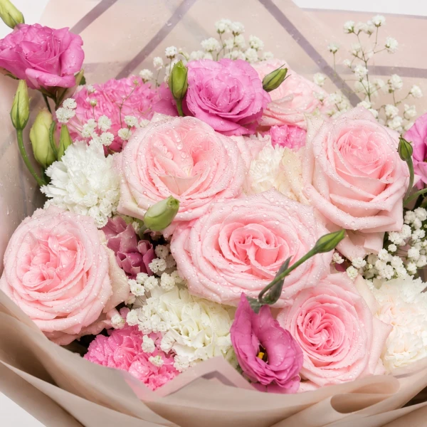 Woman in a light blue blazer holding a bouquet of pink and white roses and gypsophila.