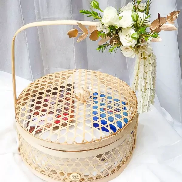 Round woven bamboo basket with lid, filled with food, topped with white flowers and a jasmine garland.