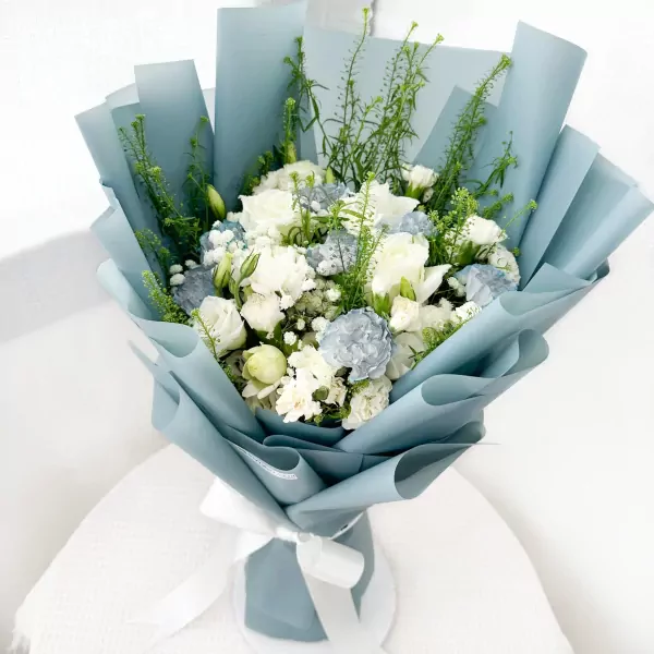 A light blue bouquet of white carnations, roses, lisianthus, and gypsophila tied with a white ribbon.