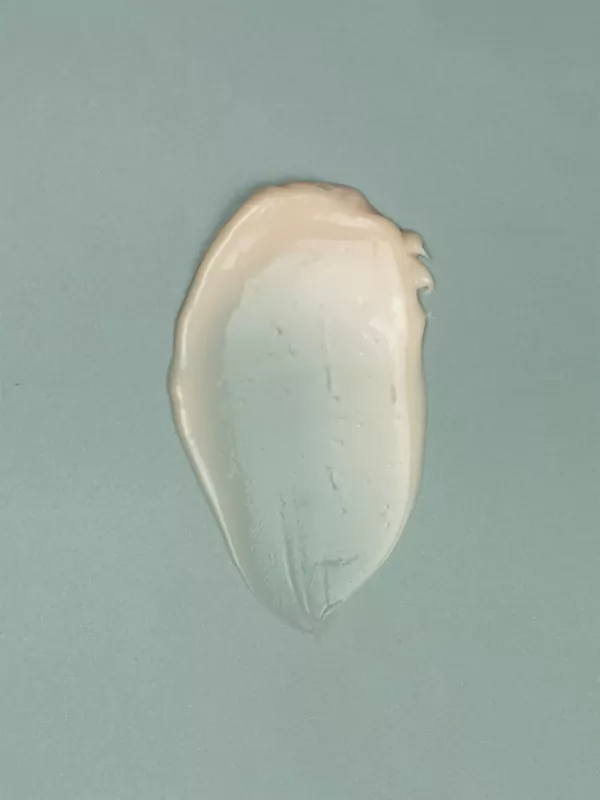 A smear of pale peach body lotion on a muted blue background.