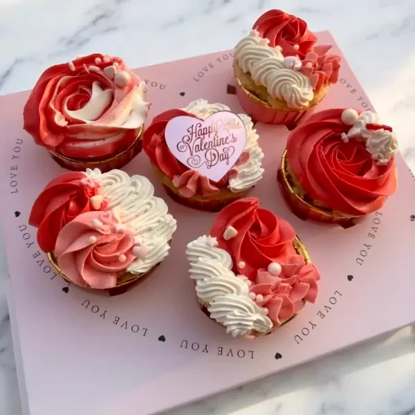 Six vegan Valentine's Day cupcakes with pink and white frosting, arranged on a pink tray.