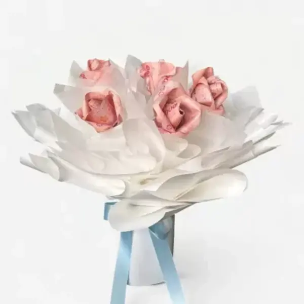 A bouquet of roses made from pink banknotes, wrapped in white tissue paper, tied with light blue ribbon.