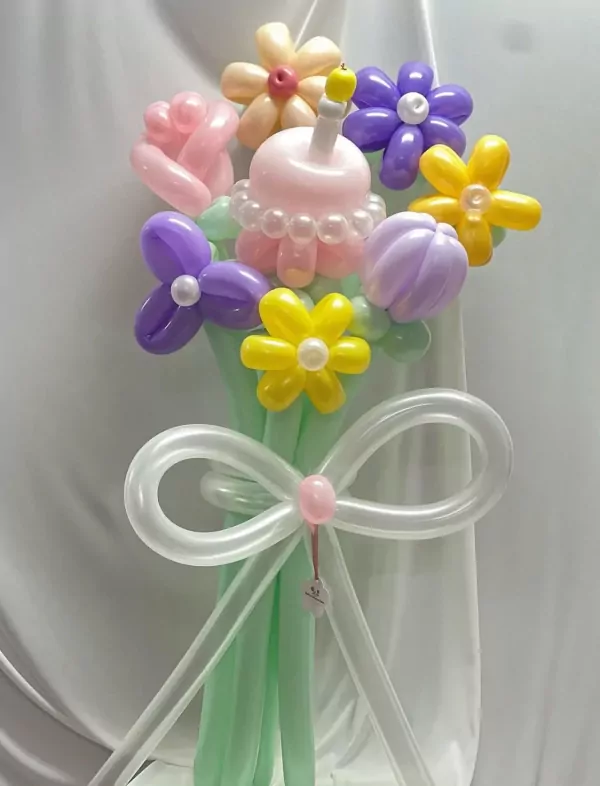 Balloon cake bouquet with colorful flowers, a candle, and a white bow.