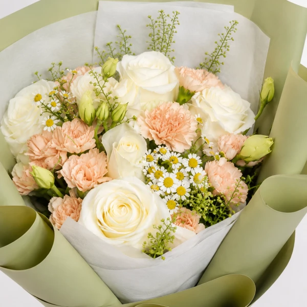 A bouquet of white and pink roses with small white flowers, wrapped in pale green paper and tied with a cream ribbon.