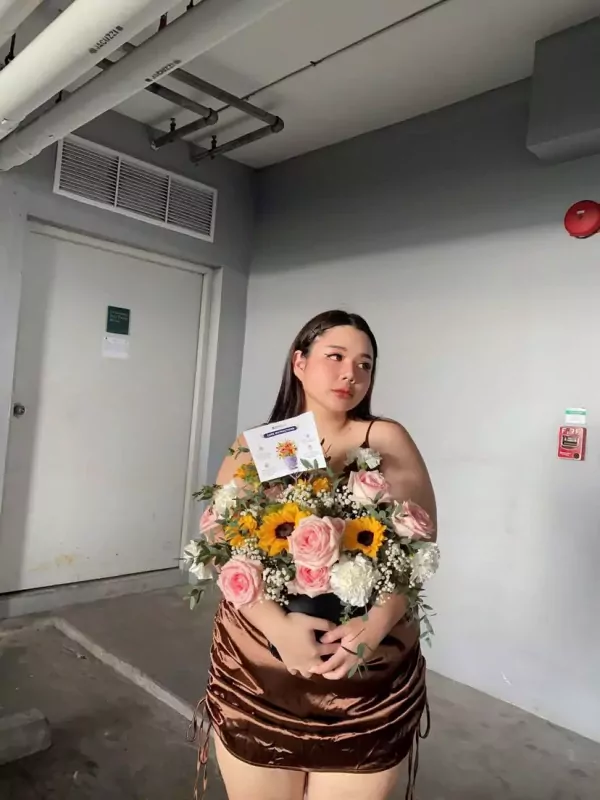 A woman holds a "Little Happiness Box" flower arrangement with sunflowers and pink roses.