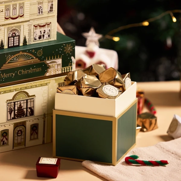Christmas chocolate box filled with gold-wrapped chocolates, with luxury manor-themed boxes in background.