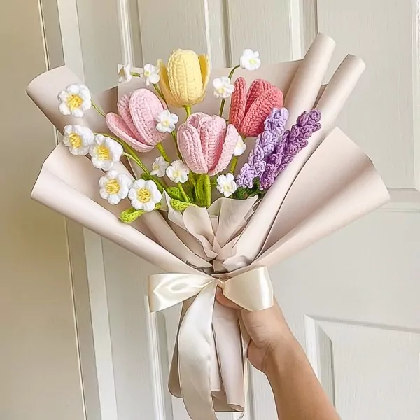 Crocheted bouquet of pink, yellow, and red tulips with white daisies and purple sprigs, wrapped in pale paper and tied with a ribbon.