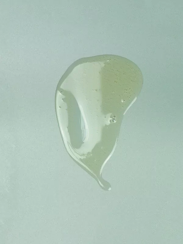 A viscous, translucent light green liquid dollop with air bubbles against a muted light blue background.