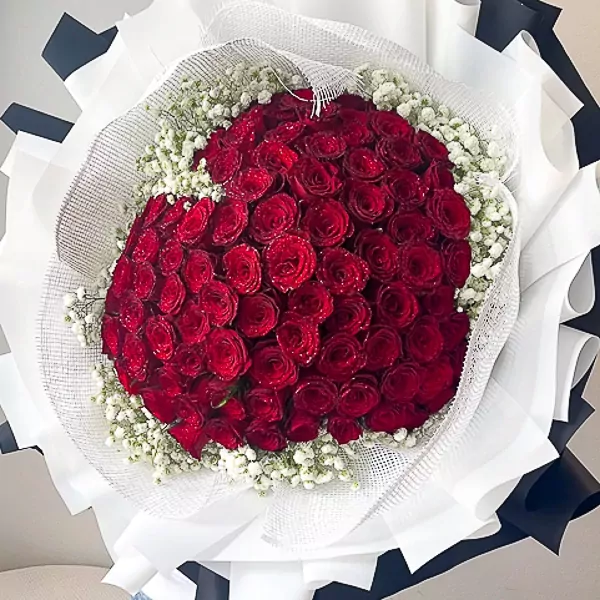 Bouquet of 99 vibrant red roses and white gypsophila flowers, artfully arranged and wrapped.