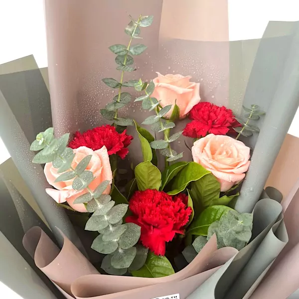 Bouquet of pink roses, red carnations, and eucalyptus leaves, wrapped in grey and pink paper.