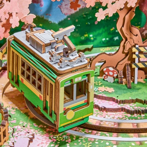 Green tram model on wooden tracks with cherry blossoms, a tree, and a mushroom.