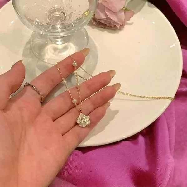 Gold necklace with rose pendant and pearls on a hand.