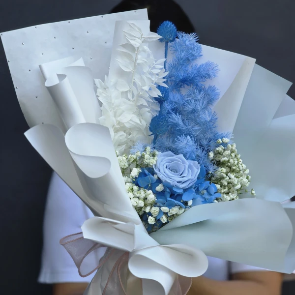 Blue and white dried flower bouquet with a light blue rose centerpiece, elegantly wrapped.