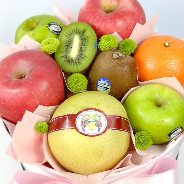 Round fruit box with apples, kiwi, orange, and pear, decorated with green flowers.