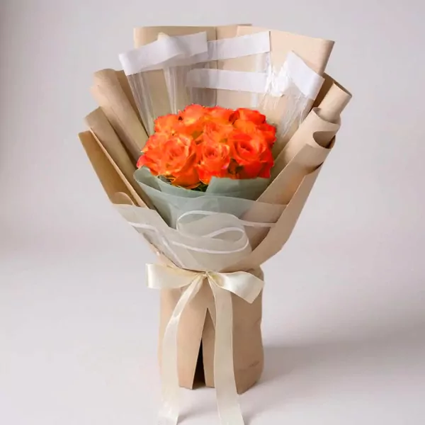 Bouquet of vibrant orange roses wrapped in brown paper with a cream ribbon bow.