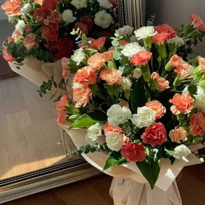 A bouquet of orange and white carnations in a cream wrapper with eucalyptus.