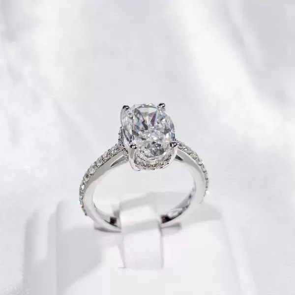 Silver oval-cut moissanite ring with paved band on a white stand.
