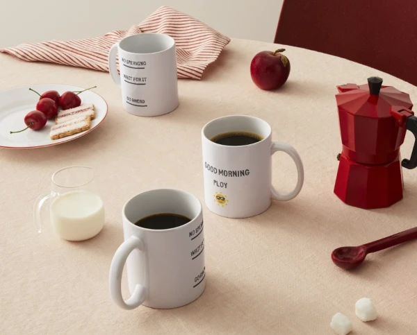 Mugs with "Good Morning Ploy" and "No Speaking" text sit on a table with cherries, cookies, milk, and a red moka pot.