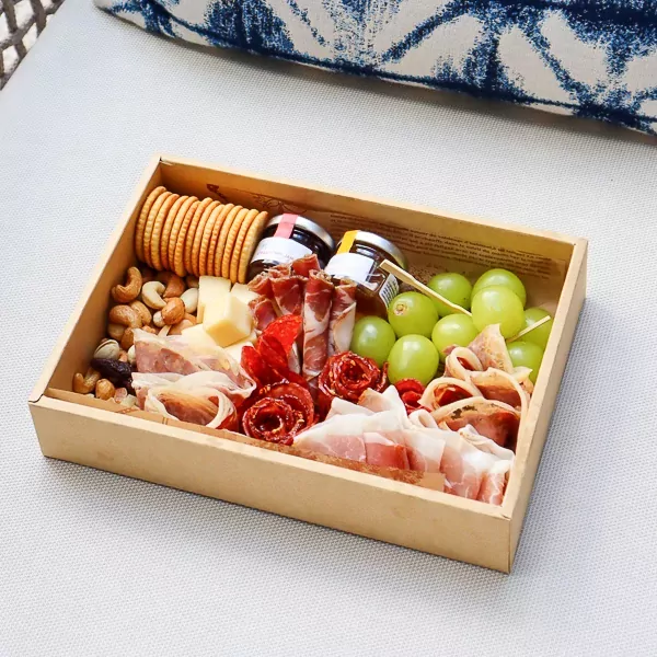 Charcuterie box with meats, cheeses, crackers, grapes, nuts, and jams on a light surface.