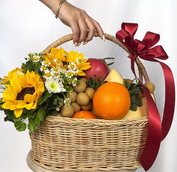 A fruit basket with sunflowers, daisies, oranges, apples, and longans, tied with a red ribbon.