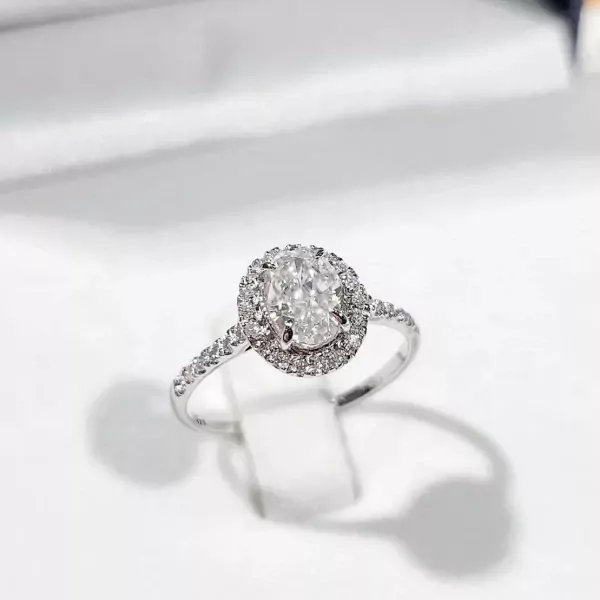 Oval moissanite engagement ring with a halo of small diamonds on a white gold plated sterling silver band.