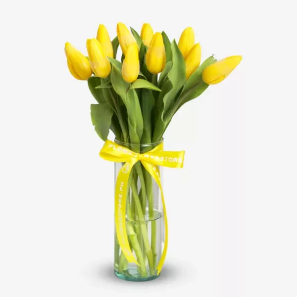 Yellow tulips arranged in a clear glass vase with a yellow ribbon tied around it.