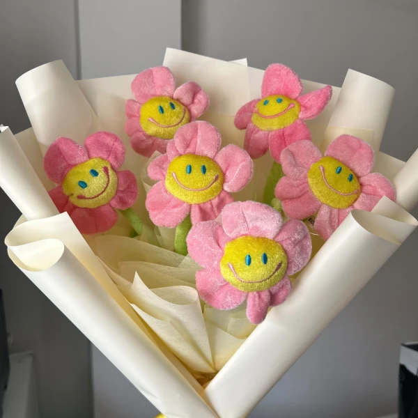 Pink plush daisies with smiling faces in a cream paper bouquet.