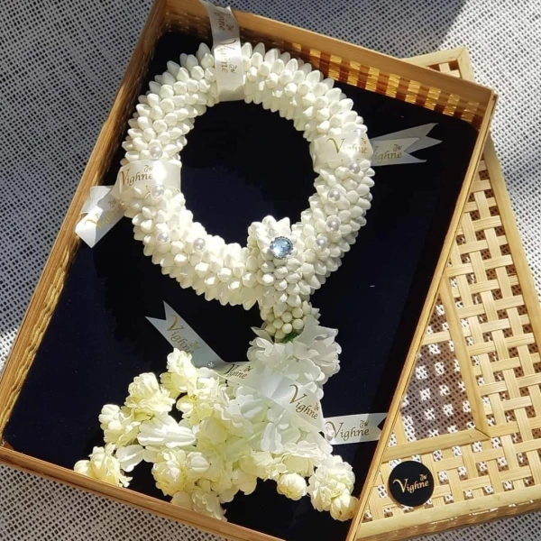 Artificial jasmine garland with pearls and blue gem in a woven basket.