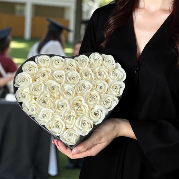 Heart-shaped box of cream roses with diamond centers, held by a person in a graduation robe.