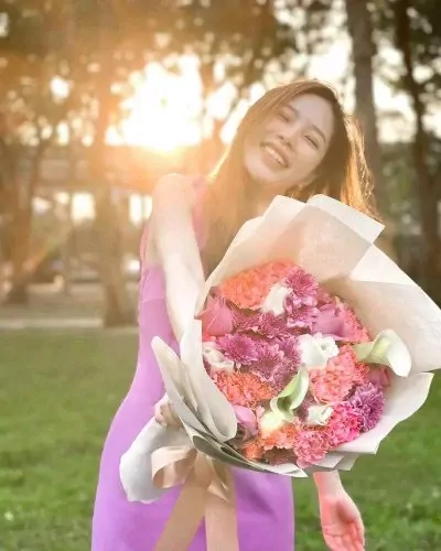 Woman in purple dress smiles holding a bouquet of pink, orange, and white flowers.