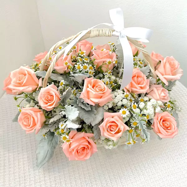 A woven basket overflowing with soft pink roses, baby's breath, and daisies, tied with a white ribbon.