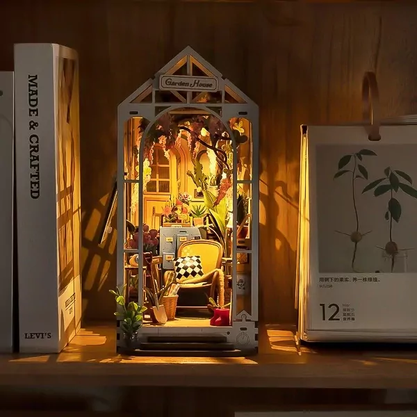 Miniature greenhouse book nook with chair, plants, and lights on a shelf.