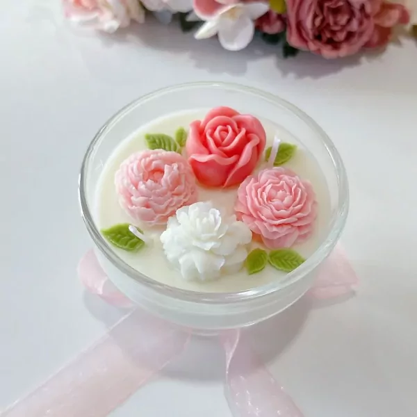 Candle in a glass bowl with carved floral wax art, including pink roses and white flowers.