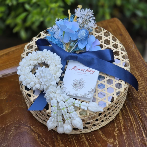 Blue artificial garland and flowers in a bamboo basket, with a blue ribbon and small card.