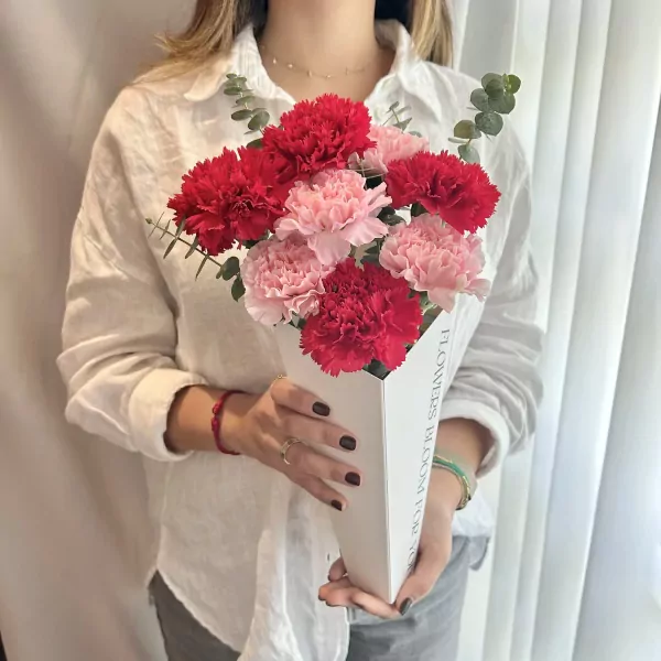 Woman holding a vase of red and pink carnations, "FLOWERS BLOOM FOR YOU" text visible on the vase.