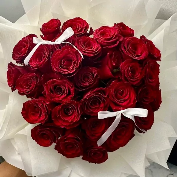Heart-shaped bouquet of 30 vibrant red roses with white ribbon accents.