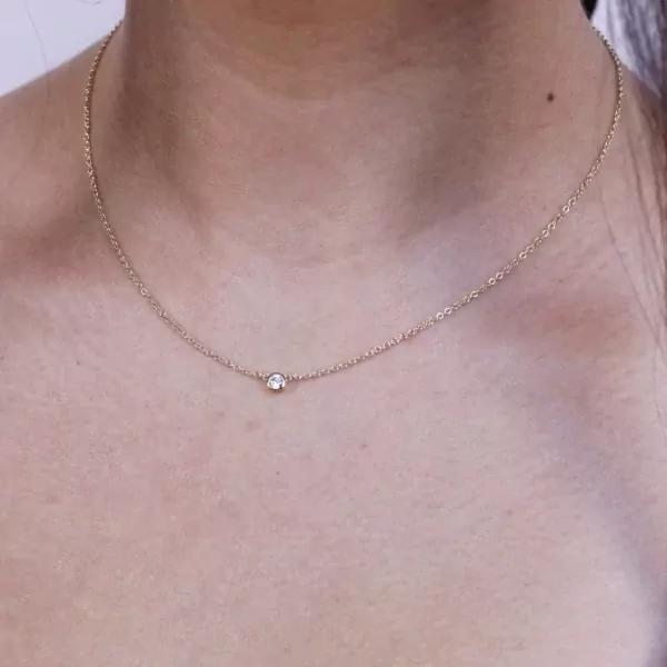 Gold chain necklace with a solitaire bezel moissanite diamond pendant on a woman's neck.