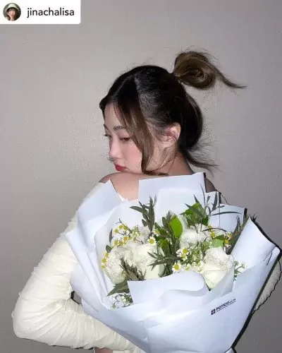 Woman with a messy bun holding a white rose and daisy bouquet.
