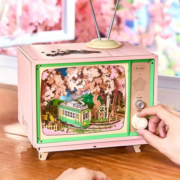 Pink vintage TV music box with a 3D scene of a green tram and cherry blossoms inside.