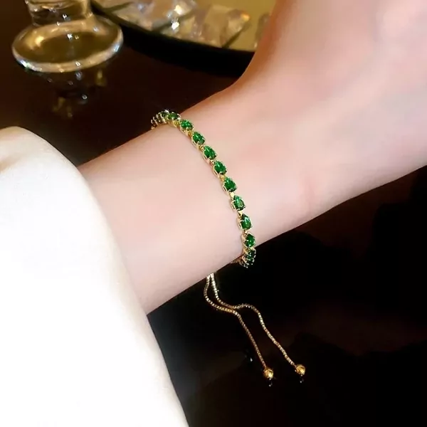 Gold bracelet with pear-shaped green emeralds on a woman's wrist.