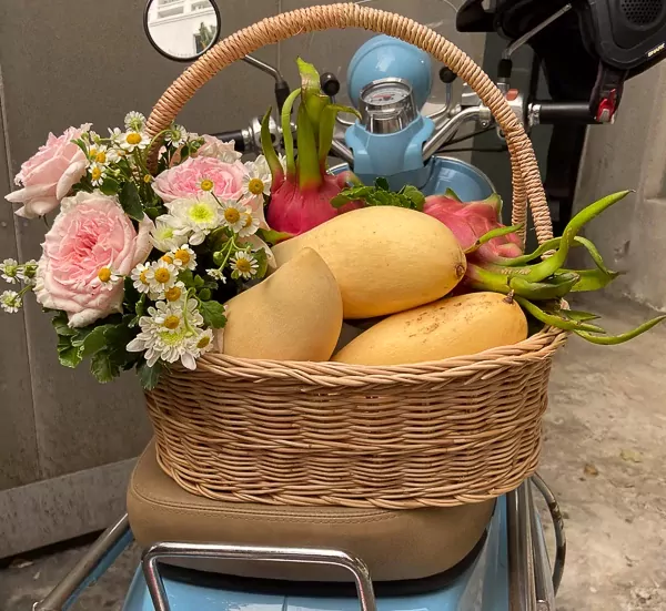 Fruit basket with mangoes, dragon fruits, and pink roses on a blue scooter.