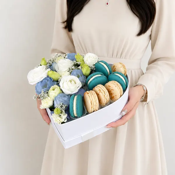 Heart-shaped box with blue and white flowers and aqua and vanilla macarons.