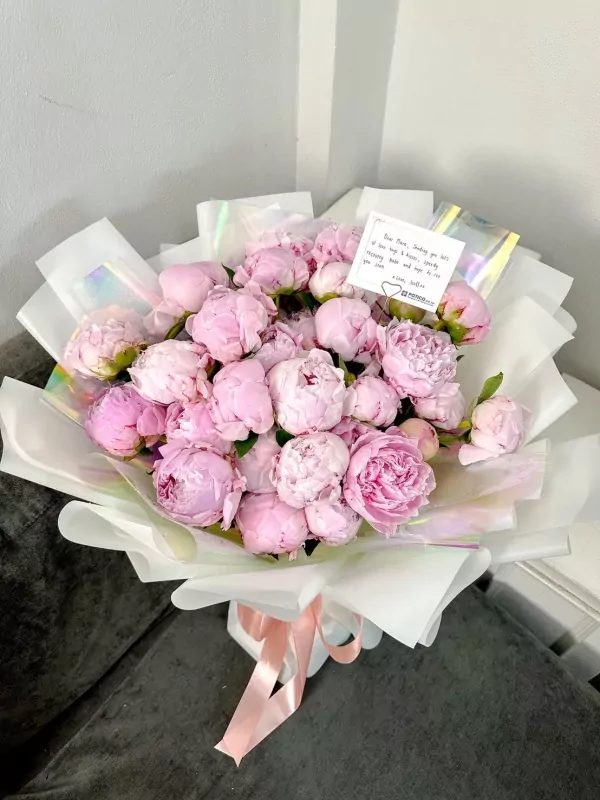 A lush bouquet of 30 pink peonies, artfully arranged and tied with a peach ribbon.