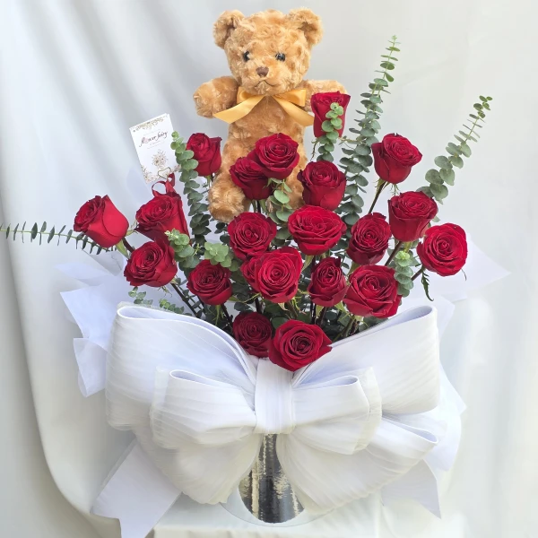 Teddy bear and red roses arranged with a large white bow, for a romantic gift.